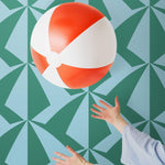 Parasol wallpaper is designed with overlapping shapes of multicolored beach umbrellas. Highly durable, fade resistant, and made in the USA. This wallpaper has a green print on a light blue background and is designed in collaboration with The Aesthetics of Joy.