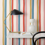 Our Picnic wallpaper was inspired by the wavy stripes of a picnic blanket. Highly durable, fade resistant, and made in the USA. This wallpaper has  blue, red , mustard yellow, and pink stripes on a blush background and was made in collaboration with The Aesthetics of Joy.