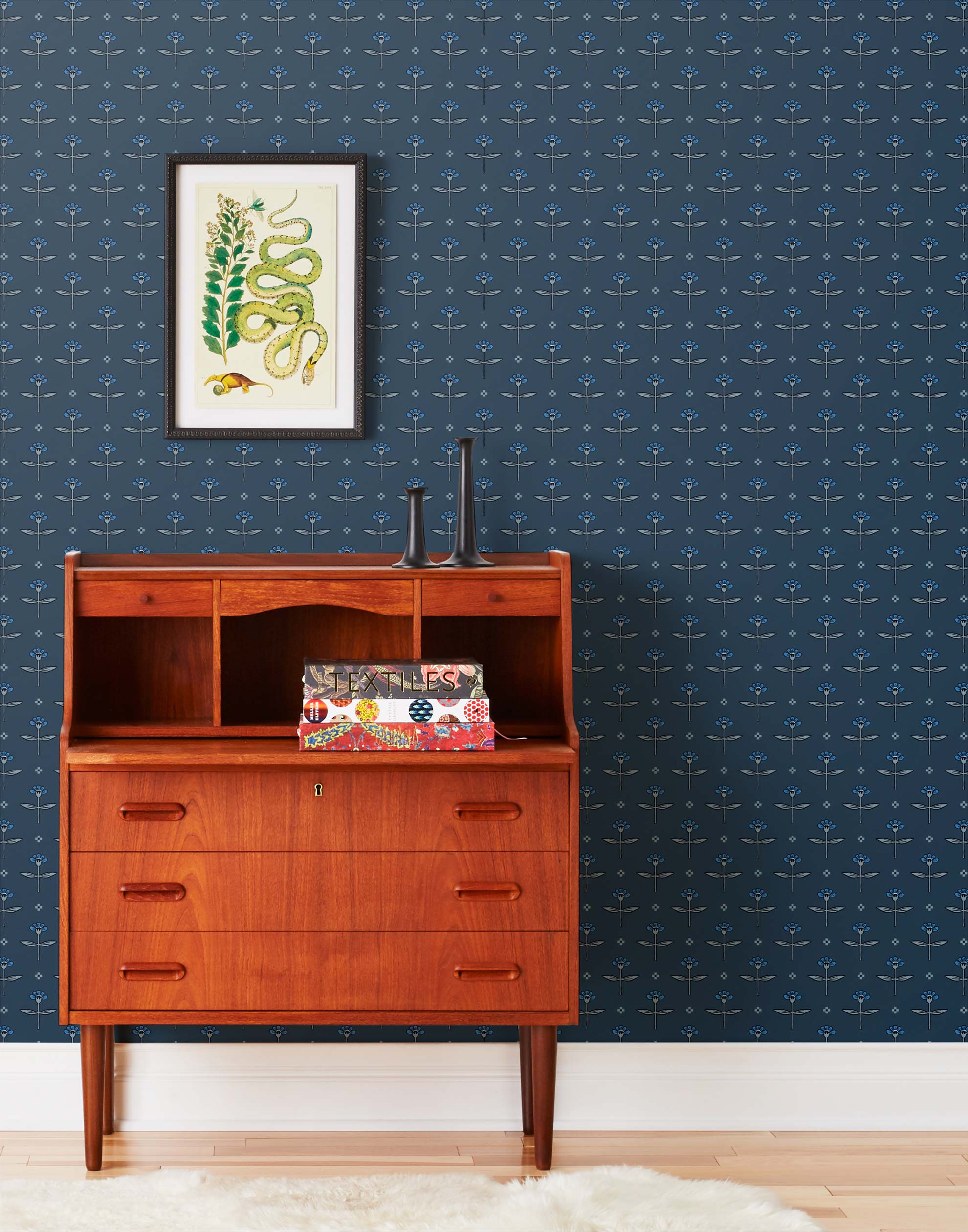 Zinnia (Indigo) Wallpaper mixes a geometric layout with the soft details of the zinnia flower. Black, gray and blue illustration on a navy blue ground.