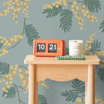Wallpaper with yellow acacia flowers and green leaves on a dusty blue background | Schoolhouse + Hygge & West