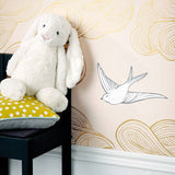 Daydream (Blush) features a pattern of flying birds and floating clouds in metallic gold and white on pink