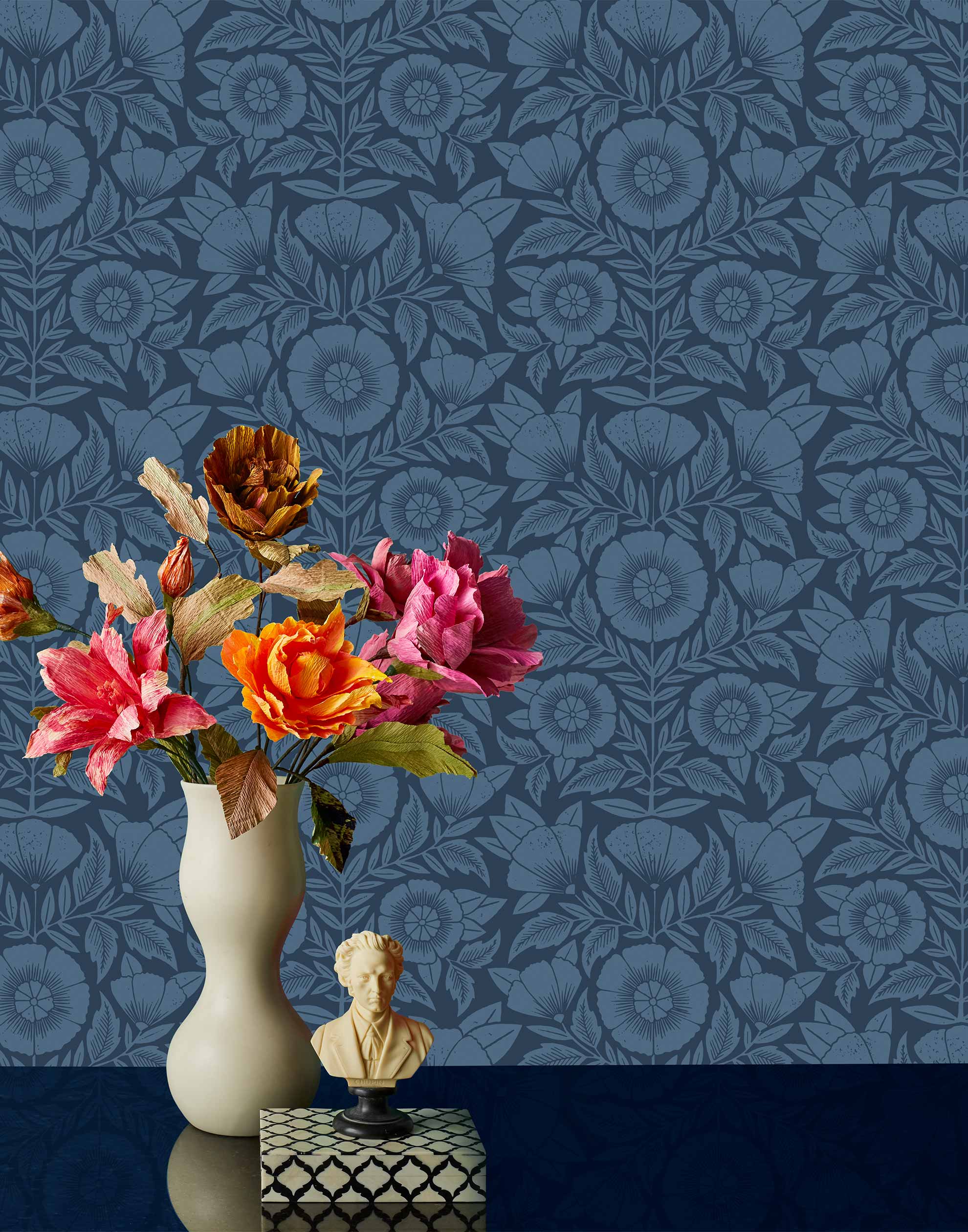 Conservatory wallpaper featuring stylized petals and leaves dervived from a block-print technique was designed by Katharine Watson for Hygge & West. Featuring cornflower blue flowers on a navy blue wallpaper background.