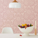 Conservatory wallpaper featuring stylized petals and leaves dervived from a block-print technique was designed by Katharine Watson for Hygge & West. Featuring light pink flowers on a rose pink wallpaper background.