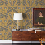 Serpentine (Butterscotch) Wallpaper featuring charcoal and cream snakes and flowers on a golden ochre yellow background