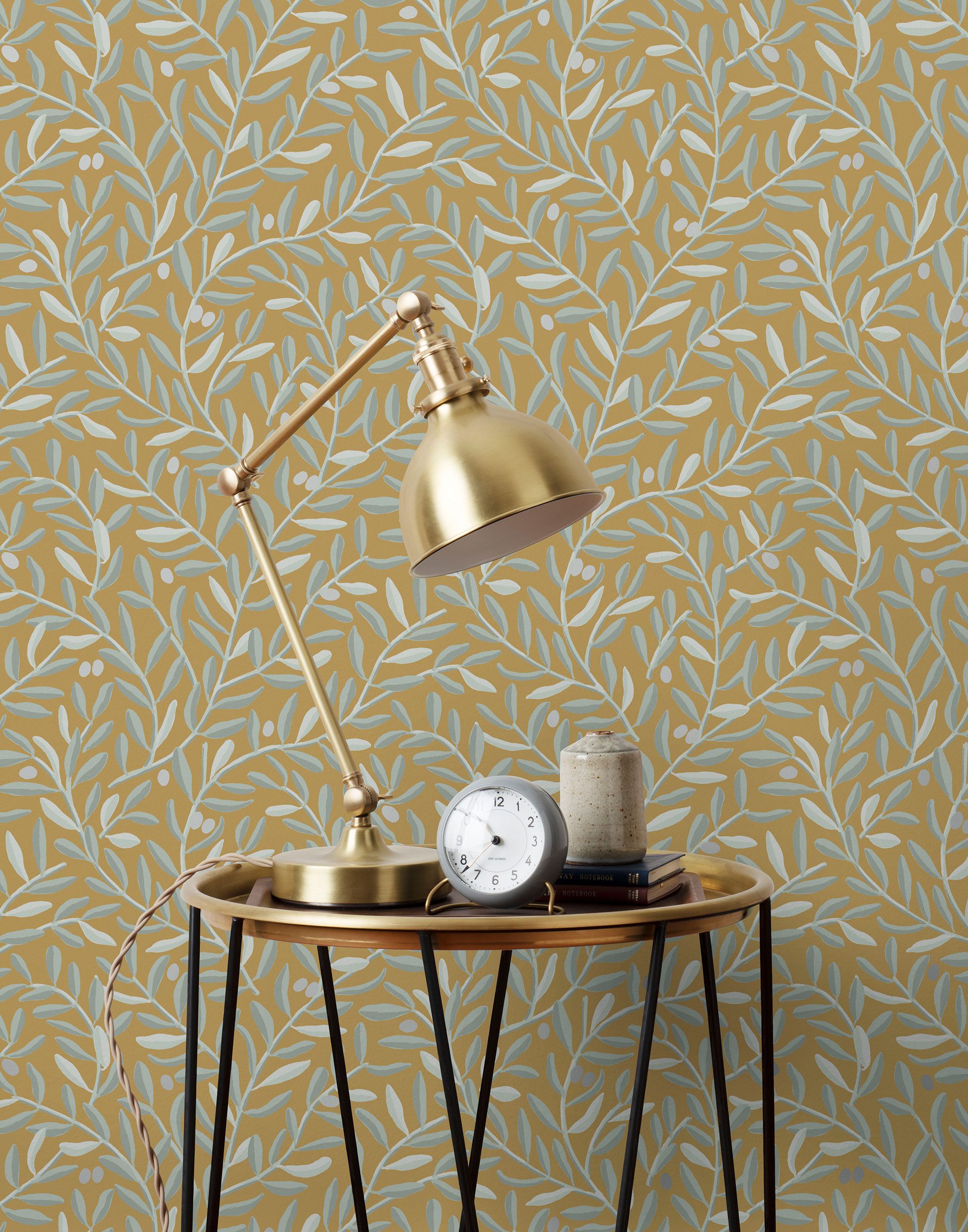 Olive Grove (Ochre) featuring a leafy vine motif in shades light green with metallic silver accents on a mustard yellow background | Schoolhouse x Hygge & West Wallpaper Collection