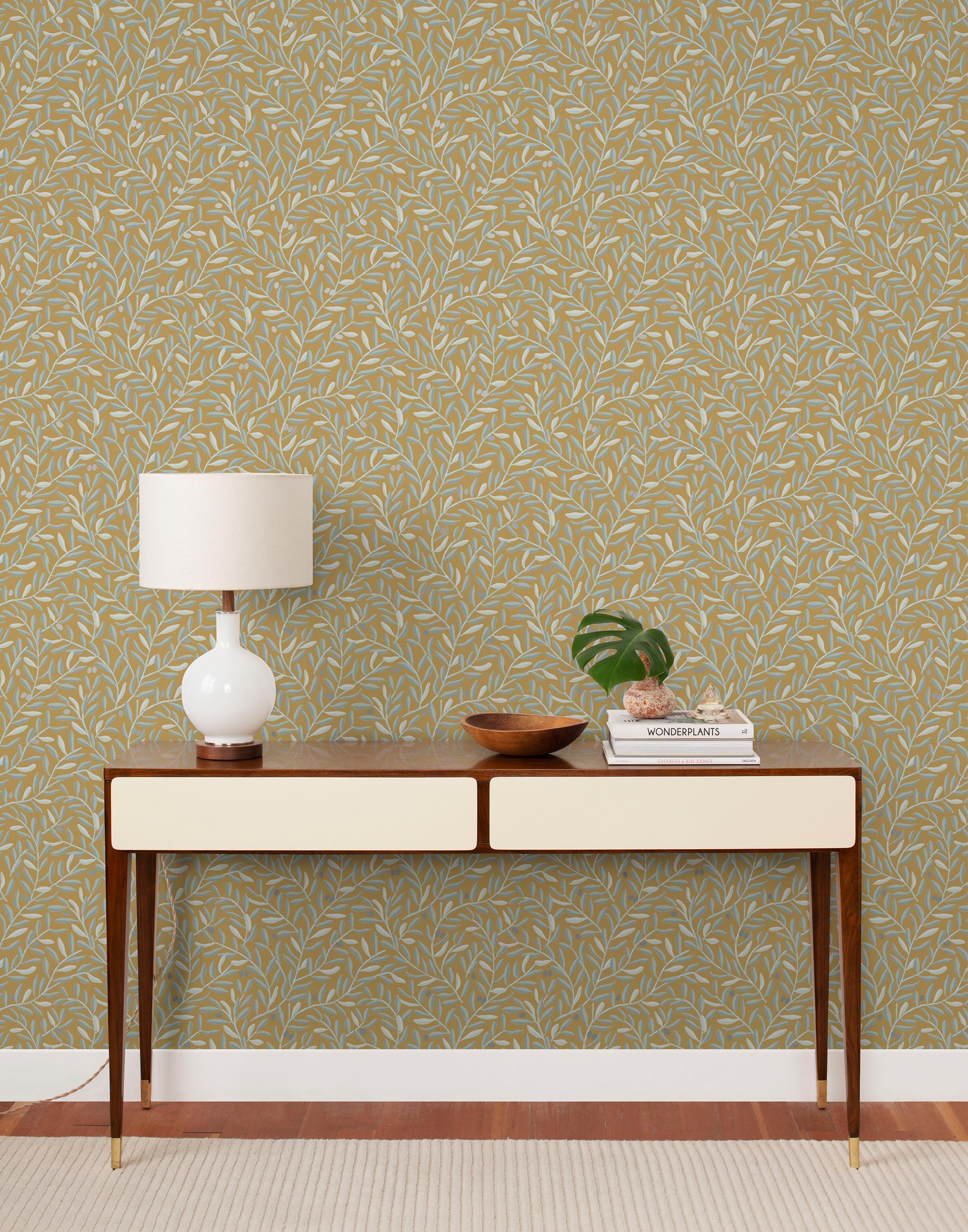 Olive Grove (Ochre) featuring a leafy vine motif in shades light green with metallic silver accents on a mustard yellow background | Schoolhouse x Hygge & West Wallpaper Collection